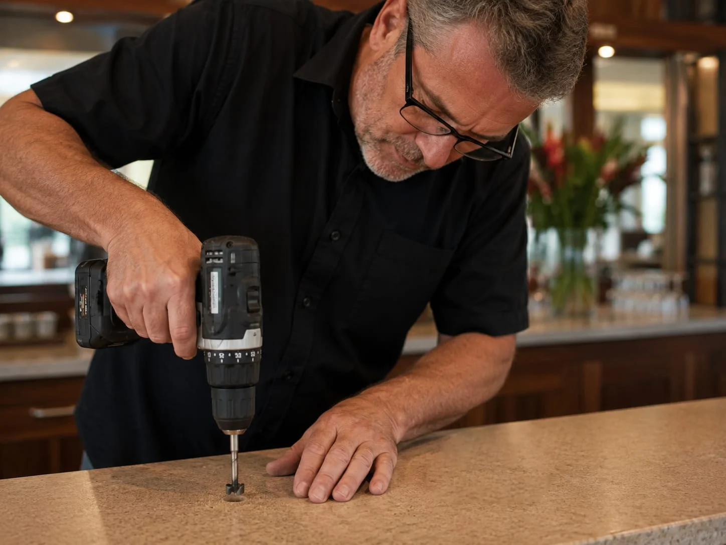 Installer drilling the small hole for a wireless charger in a stone benchtop